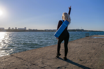 Woman Yoga Mat Beach - A woman in black leggings holds a blue yoga mat on her back while standing...