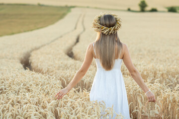 Portrait of a beautiful young woman in white dress and wreath of wheat ears in the field.
