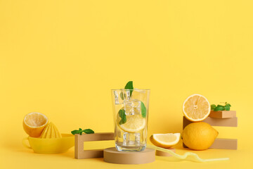 Composition with glass of lemonade, fresh sliced lemons and mint on yellow background