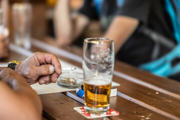 A group of friends are sitting in a pub, smoking cigarettes and drinking beer