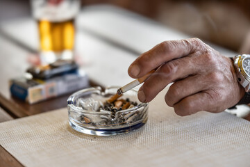 The hand of a smoking man or woman on a table led an ashtray with draft beer in a pub