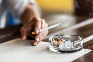 The hand of a smoking woman with a cigarette taps the ash into an ashtray