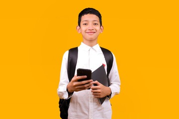 Cheerful Young Schoolboy Using Mobile Phone While Smiling Looking At Camera Over Yellow Background