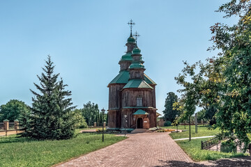 Historic wooden Holy Trinity Church with domes and Orthodox crosses, surrounded by parkland in Pustoviitivka. Fine example of Ukrainian sacred architecture. Pustoviitivka, Ukraine - June 29, 2024