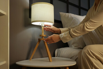 Woman turning off lamp on bedside table in bedroom at evening, closeup