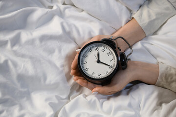 Young woman on bed holding alarm clock, closeup