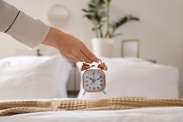 Young woman holding alarm clock over cozy bed in bedroom, closeup