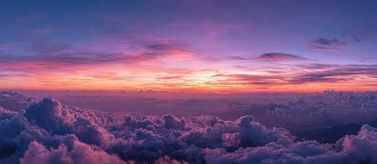 Panoramic sunset view above a sea of purple and pink clouds, with distant mountains and a vibrant, colorful sky