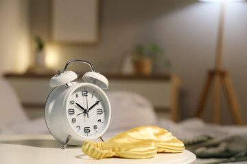 Alarm clock and sleep mask on bedside table in bedroom, closeup