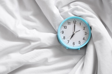 Alarm clock on bed with crumpled blanket, top view