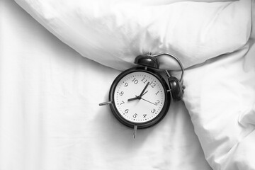 Alarm clock on bed with crumpled blanket, top view