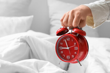 Young woman holding alarm clock over cozy bed in bedroom, closeup