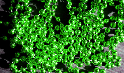 Green shiny beads are randomly placed on a black background. Macro photo. Garland. The beads are...