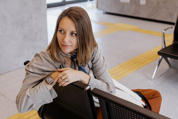 Portrait of a young woman sitting alone in a modern waiting area, looking calm and thoughtful while...