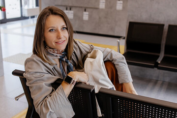 Portrait of a young woman sitting alone in a modern waiting area, looking calm and thoughtful while...