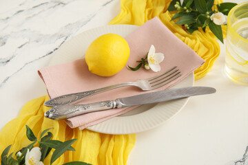 Beautiful table setting with cutlery, napkin, lemon and green branches on marble background, closeup