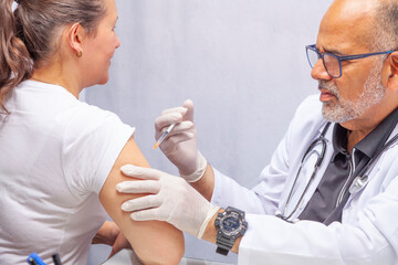 Hands of a doctor wearing white gloves administering a vaccine to a patient in a doctor's office.