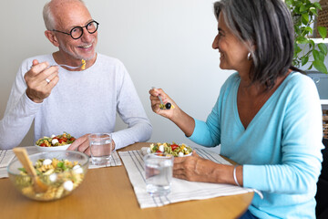 Happy mature married couple enjoying meal together at home dining table.