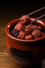 箸で持ち上げられた壺入りの梅干し