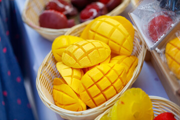 A basket of yellow mangoes with a basket of red fruit in the background