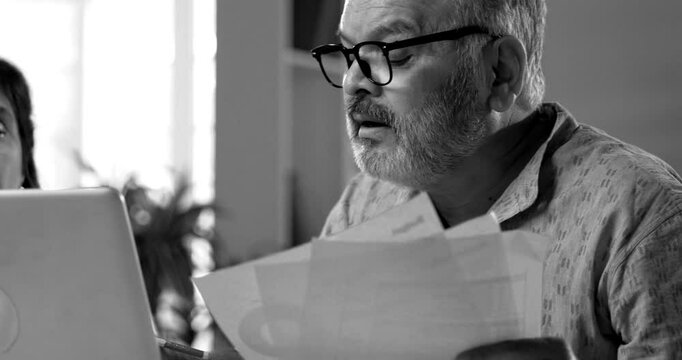 Indian couple managing home finance using laptop and documents, senior Asian husband wife reading bills calculating pension or taxes at home, planning retirement budget, digital paperwork concept - Powered by Adobe