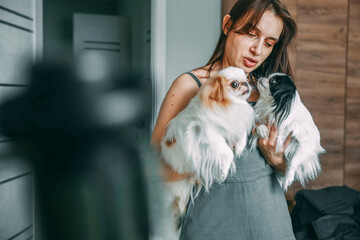 woman tenderly holding two japanese chin dogs, showcasing affection and pet care at home