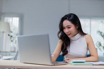 Focused young woman working on a laptop in a modern, bright office setting. She is engaged in her task, surrounded by natural light and minimalistic decor, embodying productivity and concentration