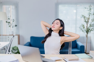 Obraz premium Woman takes a moment to stretch and relax at her desk in a modern office. She leans back with closed eyes, surrounded by a laptop, papers, and a comfortable workspace