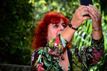 Mujer pelirroja asiéndose un selfis en el bosque