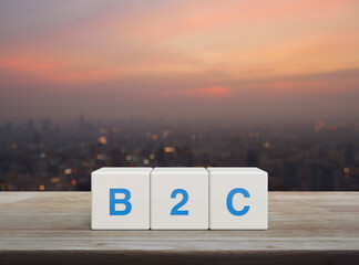 B2C acronym on white block cubes on wooden table over blur of cityscape on warm light sundown, Business to customer marketing and strategy concept