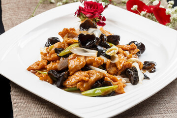 Braised pork tenderloin with scallion and wood ear mushrooms on a white porcelain plate