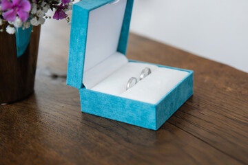 Close up of a blue box with two silver wedding rings on a wooden table, blurred background 