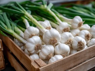 Fresh garlic bulbs with green stalks, displayed in a wooden crate, ready for sale at a market stall.