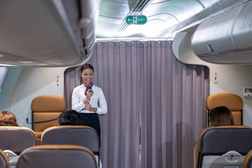 African flight attendant is greeting the passenger to welcome on board to the flight and reporting...