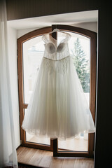 A white, fluffy wedding dress hangs on a trellis in the window