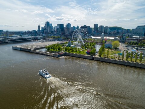 A boat cruises on the Saint Lawrence River in Montreal, Canada, offering tourists scenic views of the city skyline, La Grande Roue Ferris wheel, and waterfront park.