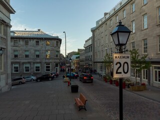 Tourists stroll along a cobblestone street in Old Montreal City, Canada. Cars navigate the steep...