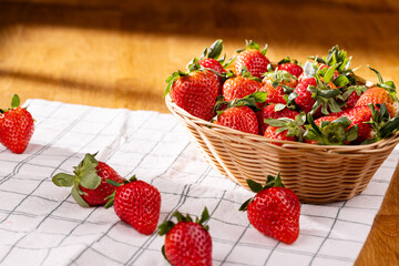 Studio shot of strawberries in a basket on a white kitchen towel with a wooden background. Bright...