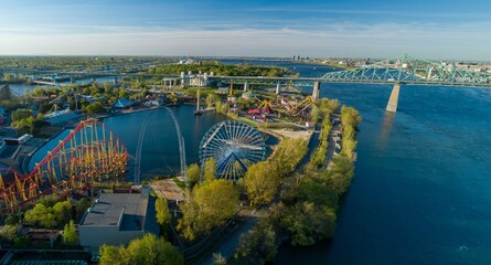 Aerial view of La Ronde amusement park in Montreal, Canada, featuring roller coasters and the Jacques-Cartier Bridge. The park provides entertainment for tourists.