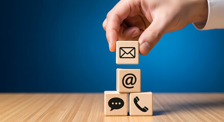 Hand stacking wooden blocks with email, at symbol, chat, and phone icons, symbolizing communication and contact methods on a wooden surface.