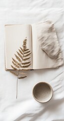Open notebook with dried fern, cloth, and bowl on white linen