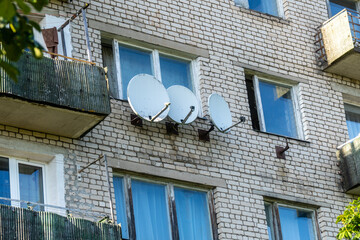 Satellite Dishes Mounted on Soviet-Era Apartment Building Facade in Residential Area. Close-Up of Multiple Satellite Antennas on Exterior Wall of Brick Apartment Block