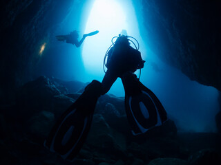 divers with flashlight diving between the rocks of an underwater cave, concept of scuba diving and...