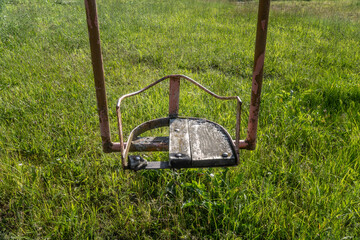 Close-up of Weathered Rusty Vintage Soviet-Era Swing Seat on Grassy Field in Rural Latvia –...