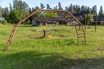 Abandoned rusty Soviet-era playground with metal climbing frame, broken swing and carousel in...