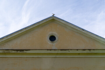 Minimalist architecture detail of a classical building gable with round window and a seagull...