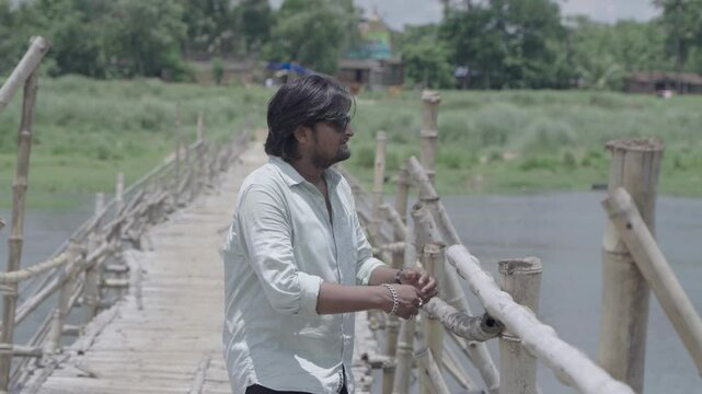 A man stands on the bamboo bridge built over the Damodar River and enjoys the natural beauty.