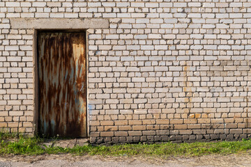 Old rusty metal door in concrete frame set into weathered white brick industrial wall, with...