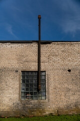 Old ventilation pipe above glass block window on weathered brick industrial wall with patina and...