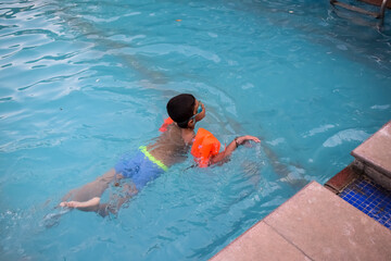Happy Indian boy swimming in a pool, Kid wearing swimming costume along with air tube during hot summer vacations, Children boy in big swimming pool.